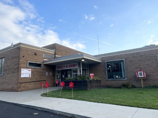 A Grizzly Academy sign hangs over the entrance to the building. This building is called the Charles R. Parsons Administrative Building. 