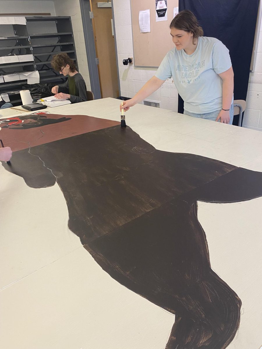 Luke Schlueter (left) and Allison Schilling (right) work on the grizzly bear mural, which will go in the weight room They typically paint after school and on weekends. Photo by Grace Sharp 