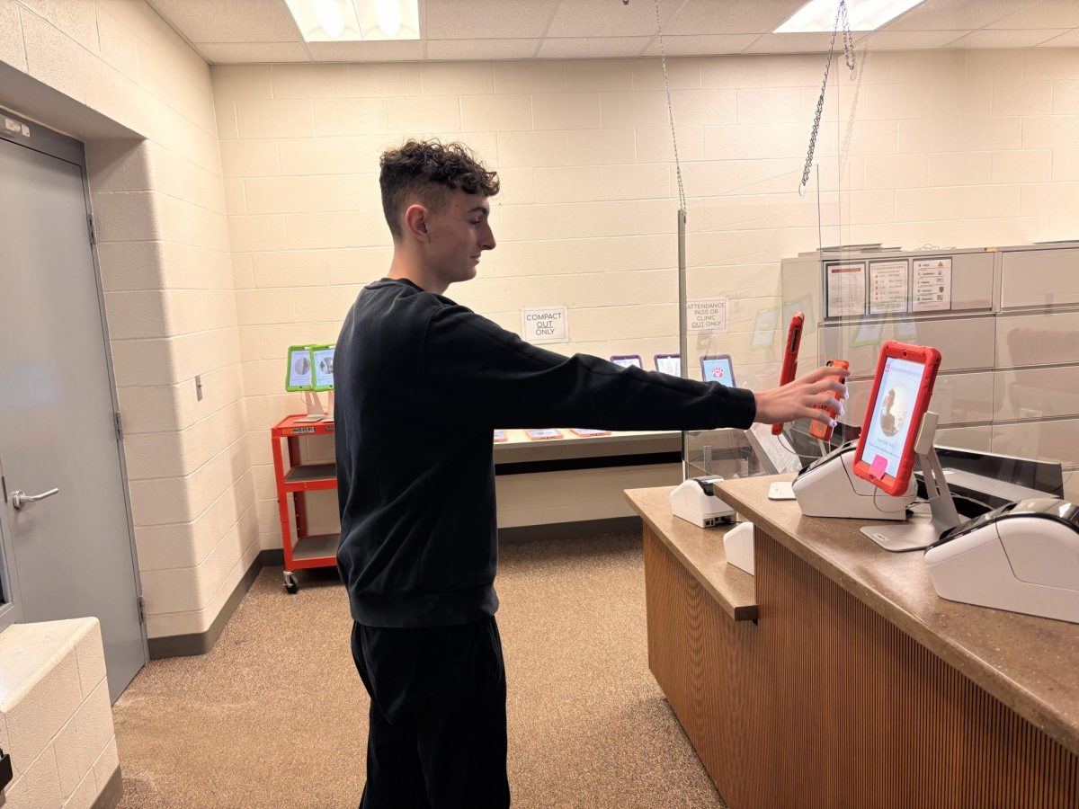 Drake Fairbanks holds up his phone to scan into school as tardy, the printer will then make a tardy pass. The attendances are measured by the attendance office, which will then be monitored by Sullivan to send out emails to parents about their children’s tardies. Photo by Henry Chen.