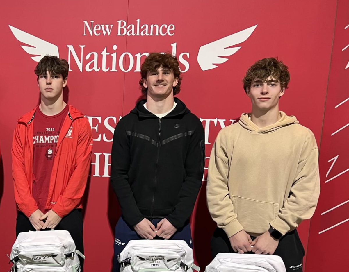 These are the following students posing with their provided backpacks in front of a New Balance Nationals sign: Alex Valentine, Calix Lemp and Cooper Gray. The backpack was provided to the athletes who compete at the New Balance Nationals track meet. Photo courtesy of Chris Beery. 
