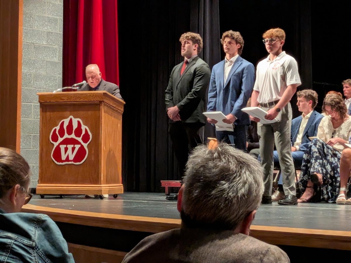 Speaker, John Gramuglia stands at a podium to present awards to members of the wrestling team. From left to right, stand Jacob Earnest, Kolten Mellon and Blake Frantz. Gramuglia awarded the wrestlers the Golden Grizzly Scholarship, Greg North Perseverance Award and the Tex Randolph Scholarship.
